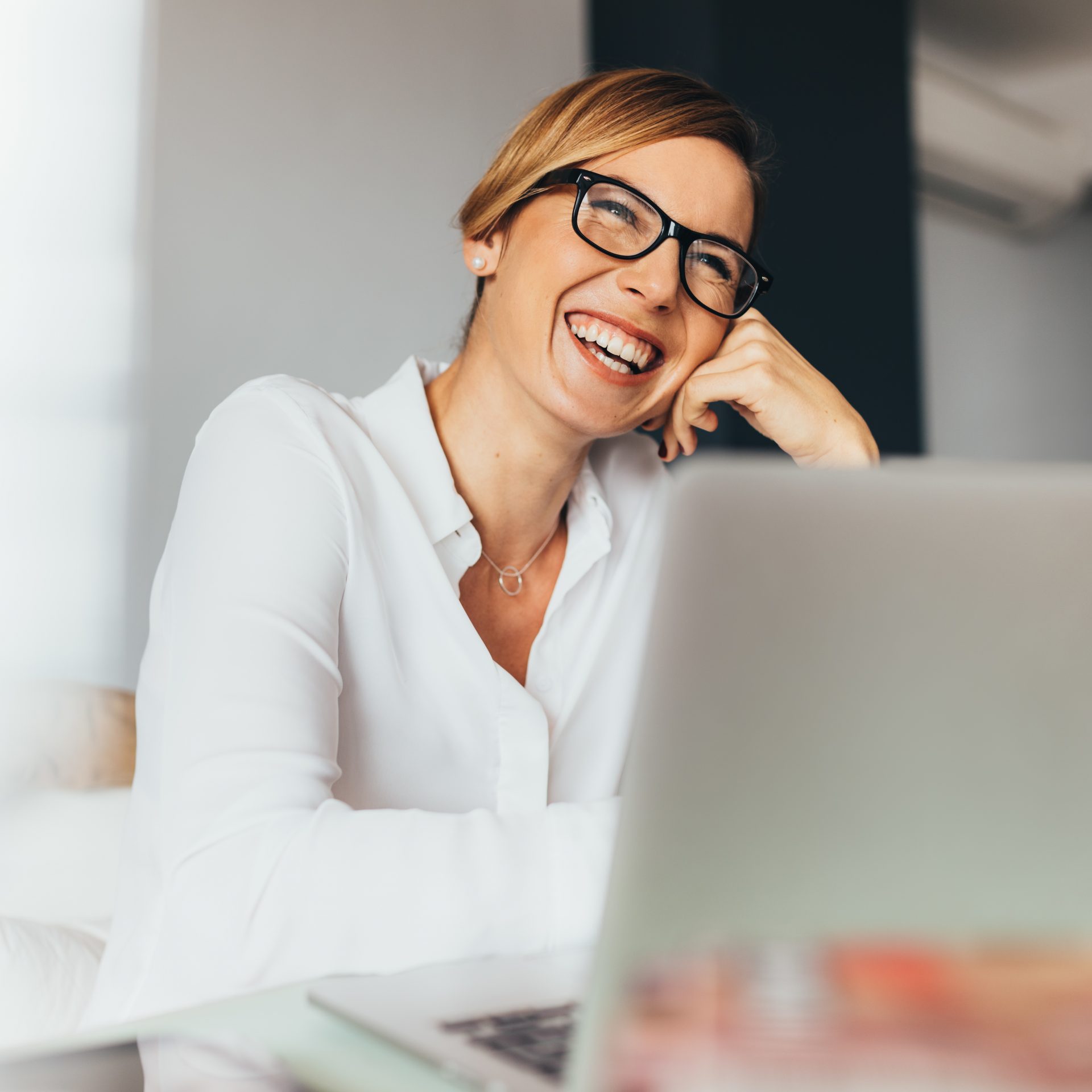 Smiling business woman in spectacles sitting at her desk in office. Woman sitting in office with laptop computer on her desk.